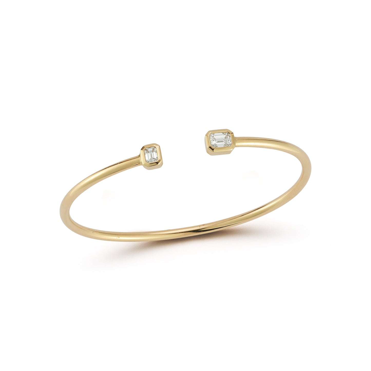 A delicate gold cuff bracelet with two small emerald bezel diamond accents at each open end is displayed against a white background, conveying elegance and simplicity.