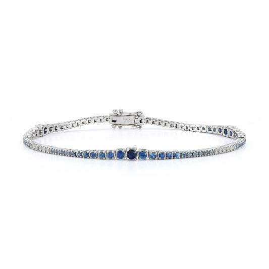 A sleek white gold bracelet with alternating blue sapphire and diamonds ombre set in a symmetrical, elegant pattern, displayed on a plain white background.