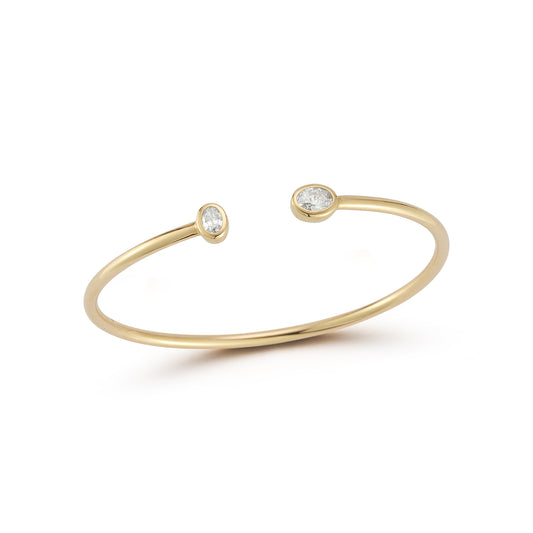A delicate gold cuff bracelet with two small oval bezel diamond accents at each open end is displayed against a white background, conveying elegance and simplicity.